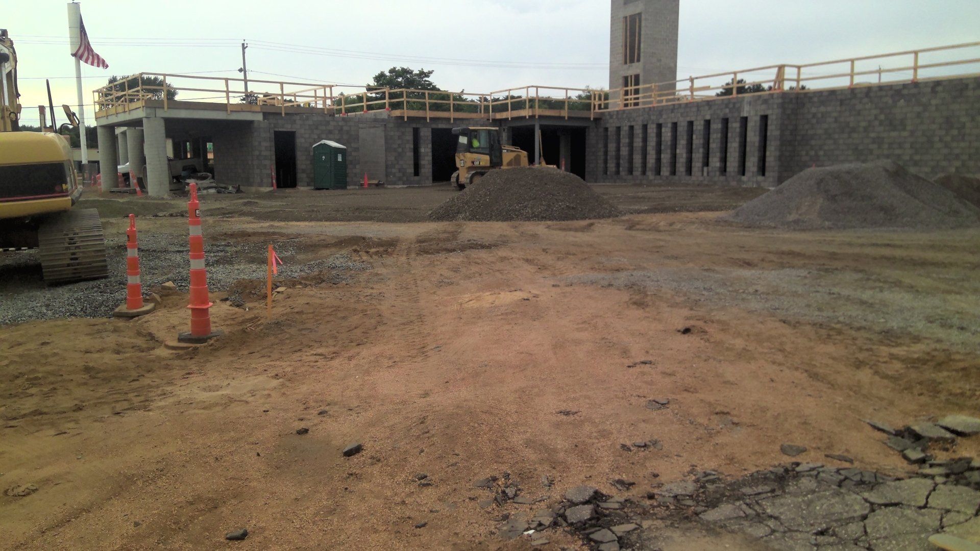 Construction site with building frame, gravel piles, and orange safety cones.