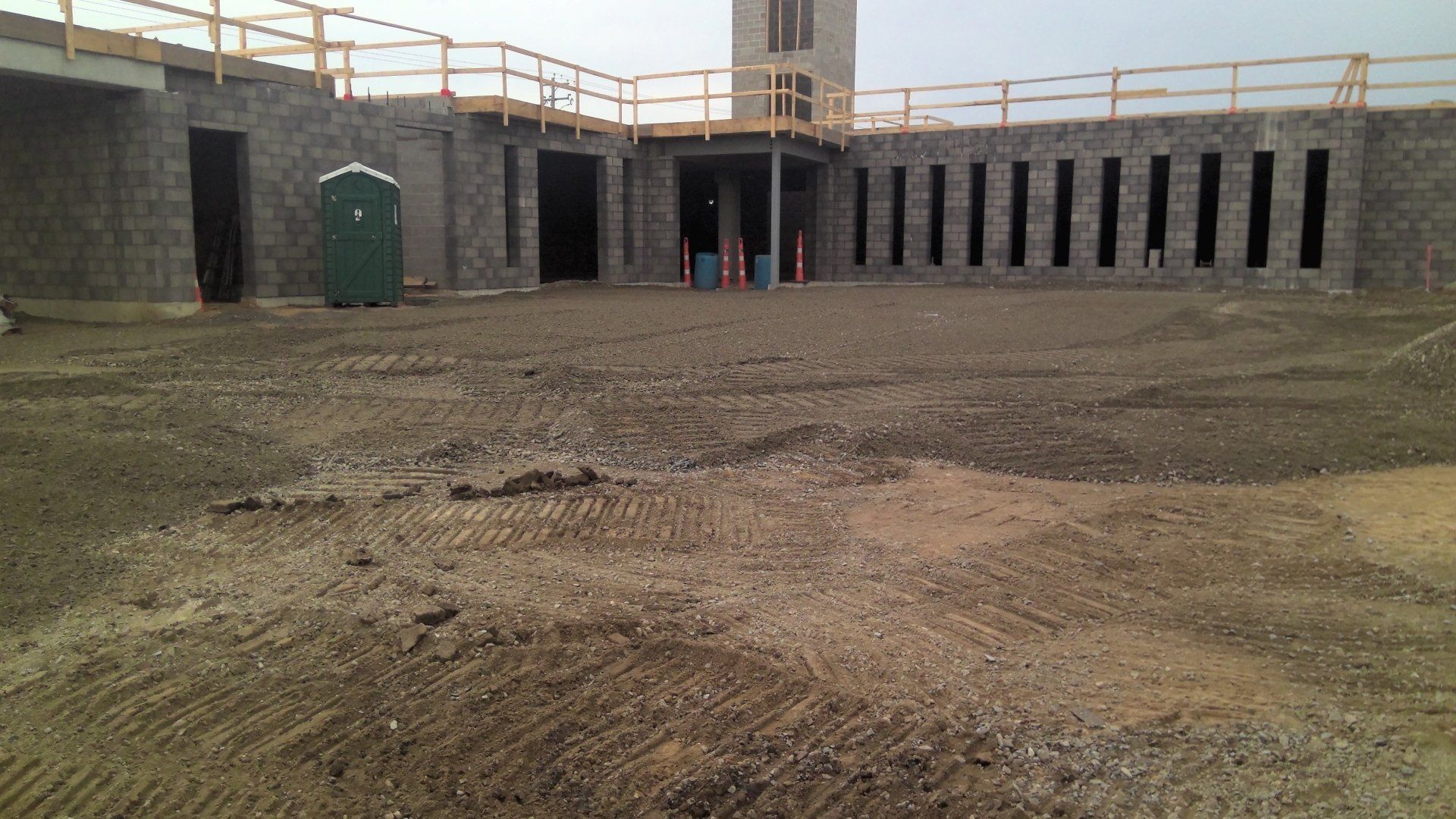 Construction site: unfinished building with exposed cinder block walls, dirt ground, and portable toilet.