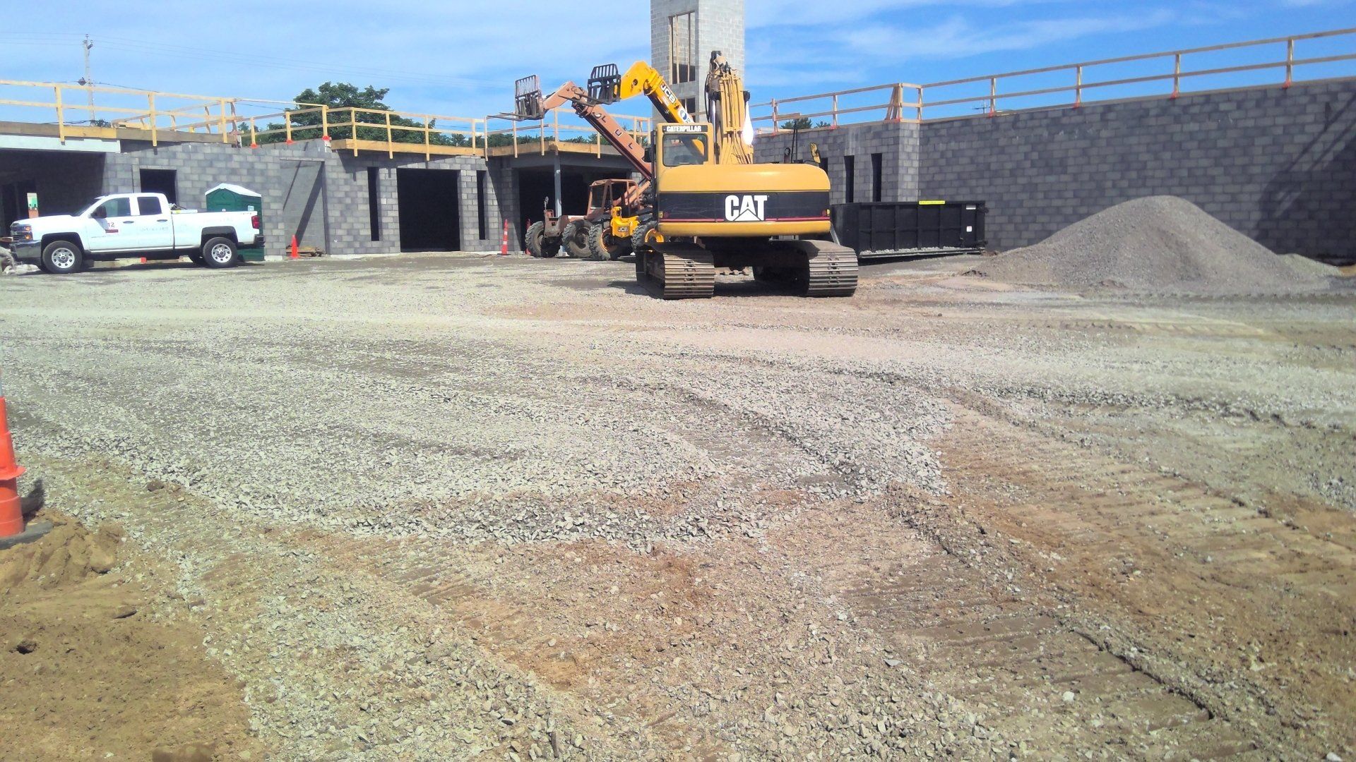 Construction site with a CAT excavator. A white truck and building under construction are also visible.