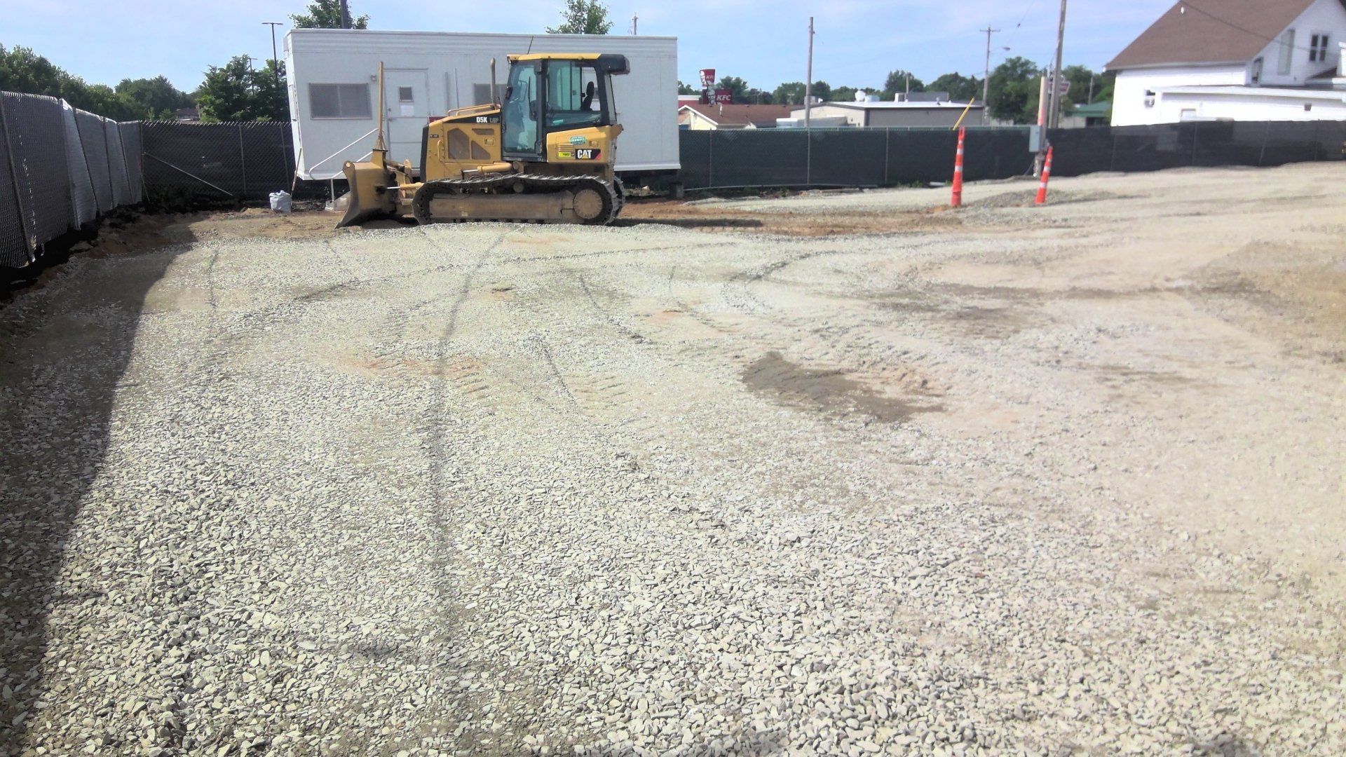 Construction site with a bulldozer on gravel, temporary fencing, and a white building.