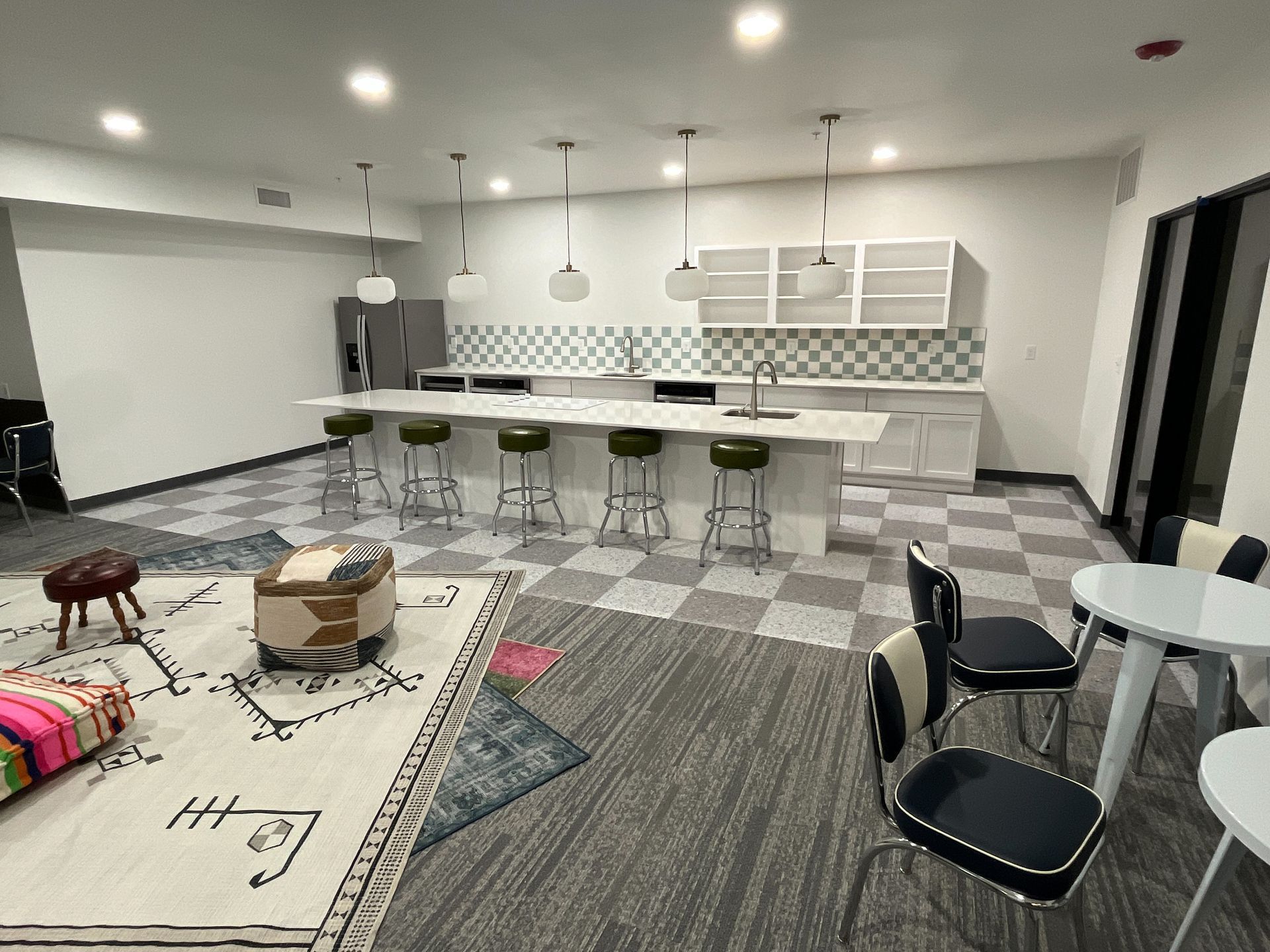 Modern kitchen/lounge area with checkered floor, large island with stools, white cabinets, and seating area with a rug.