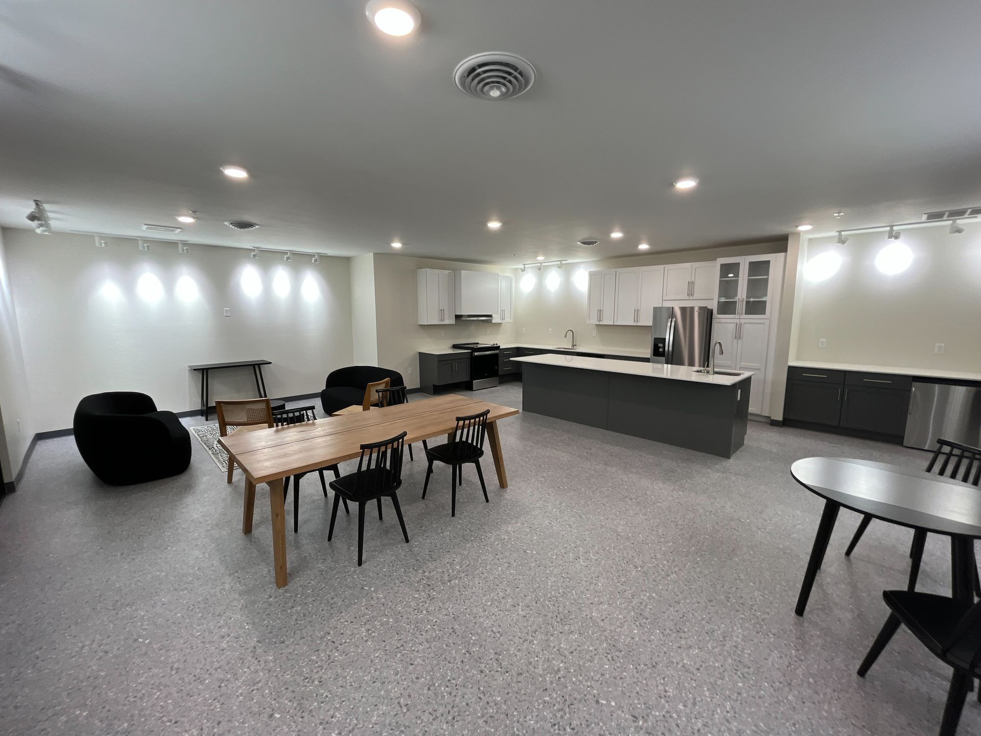 Open-concept kitchen and dining area with gray and white cabinetry, dining tables and chairs, and a beanbag chair.