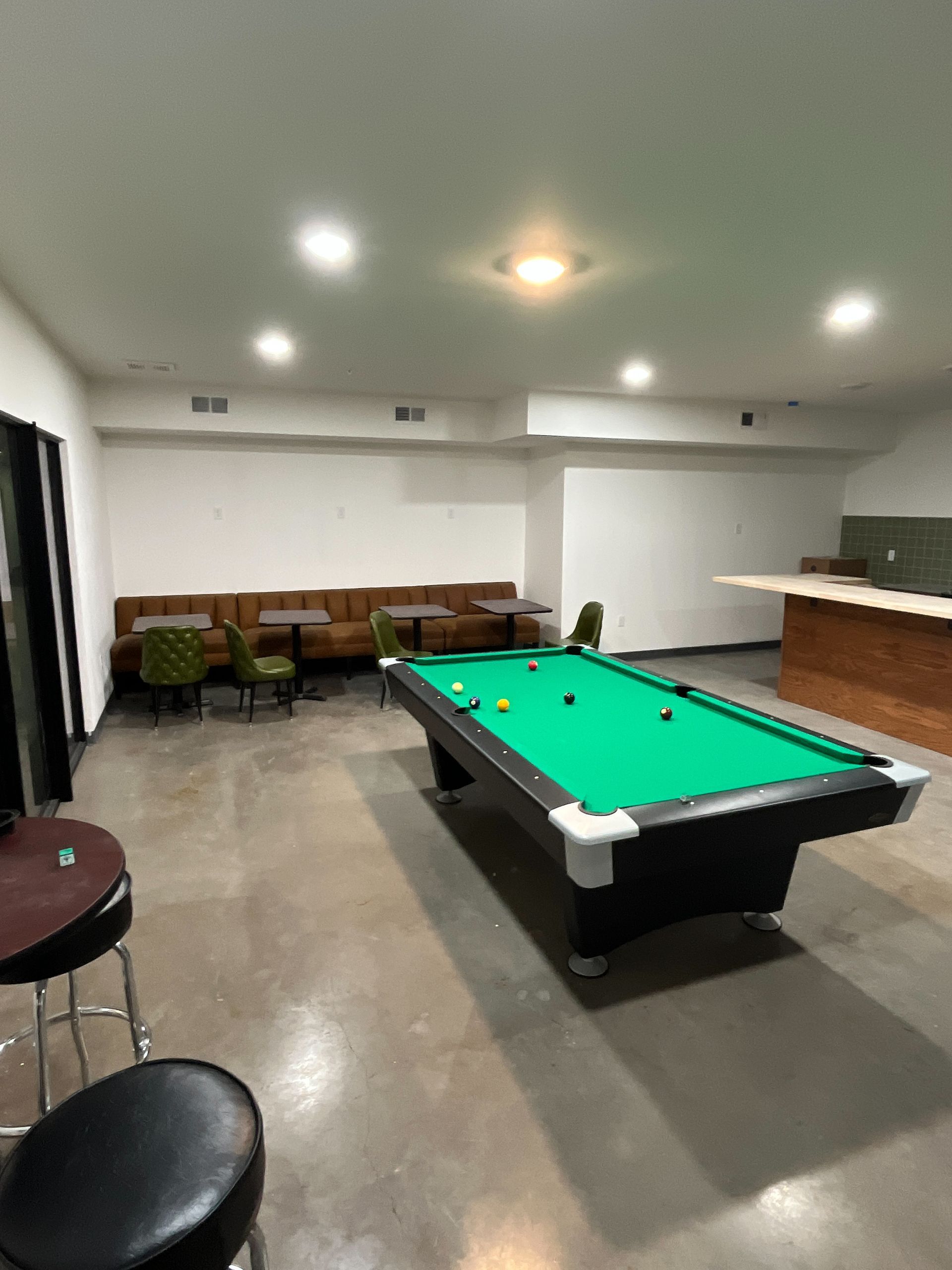 Pool table in a room with seating, bar, and overhead lighting.