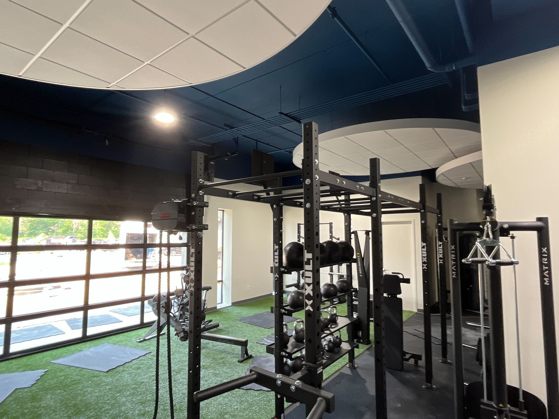 Gym interior with exercise equipment, green turf floor, and blue and white ceiling accents.