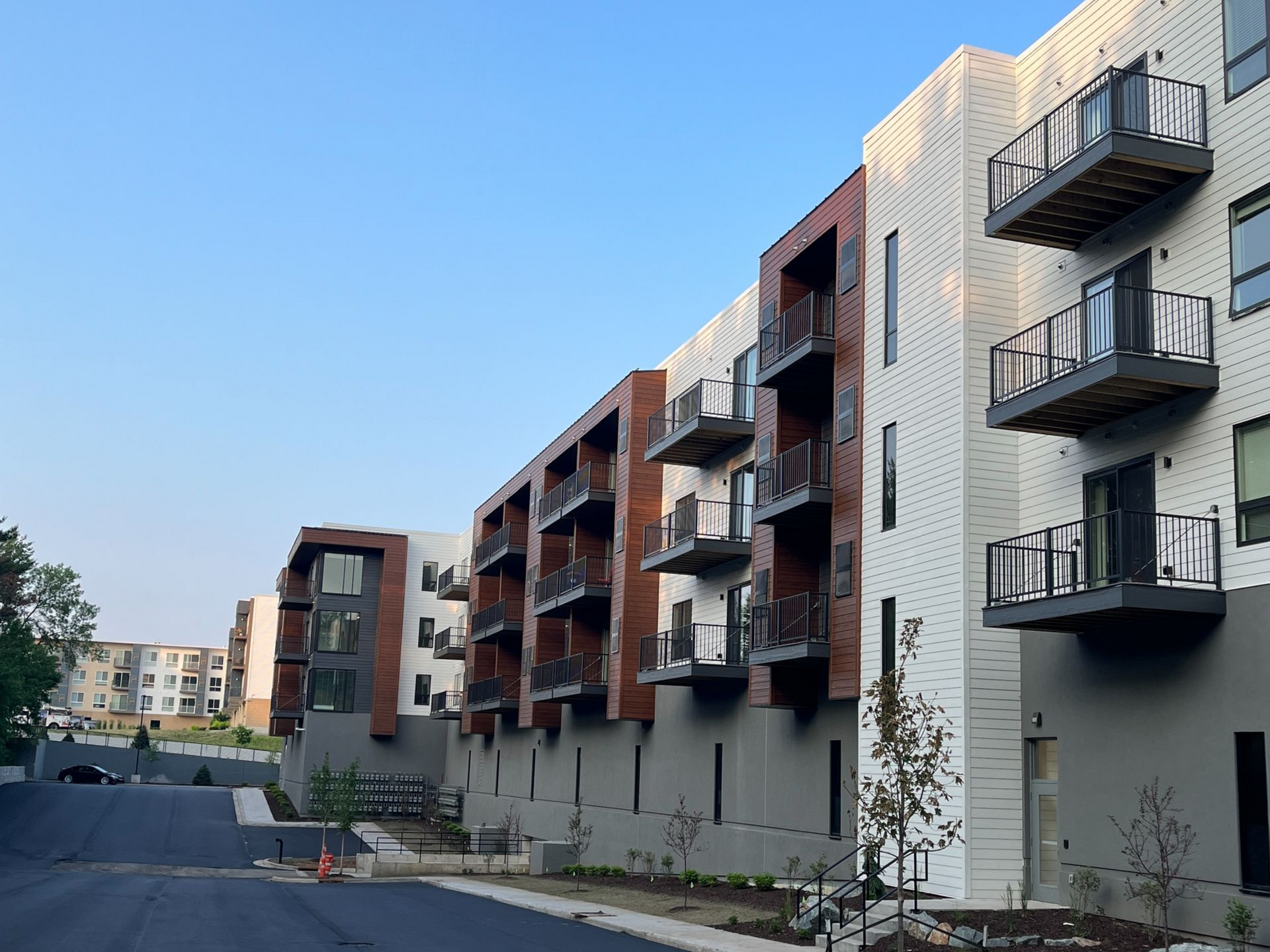 Multi-story apartment buildings with brick and metal accents, balconies, and a paved road.