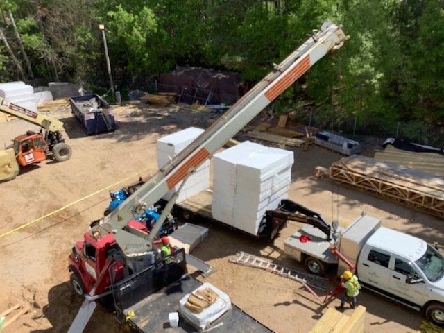 Crane lifting large white blocks from a truck at a construction site.