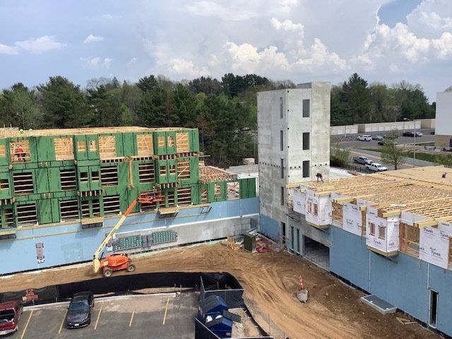Construction site with framed buildings, a concrete tower, and parked vehicles. Trees and sky in background.