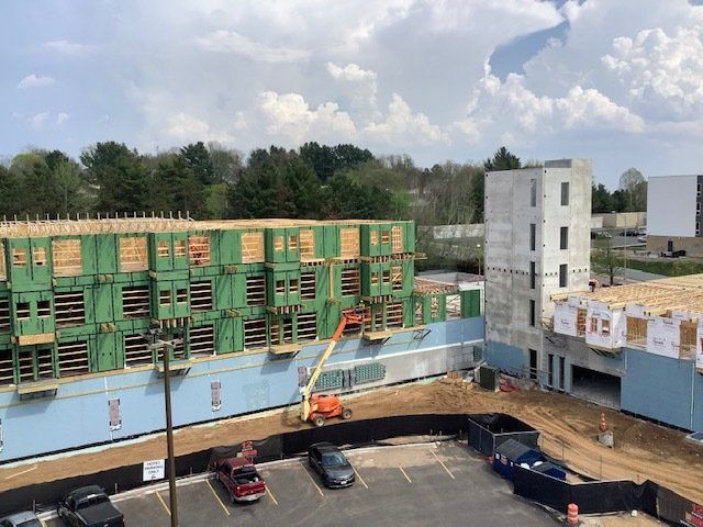 Construction site with a multi-story building frame, workers on an orange lift, and parked cars.