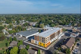 Aerial view of a multi-story apartment building with a vibrant yellow and orange accent, in a town with many trees.