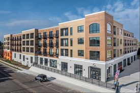 Multi-story brick apartment building with ground floor retail, blue sky.