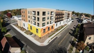 Modern apartment building on a corner lot; tan, yellow, and orange accents.