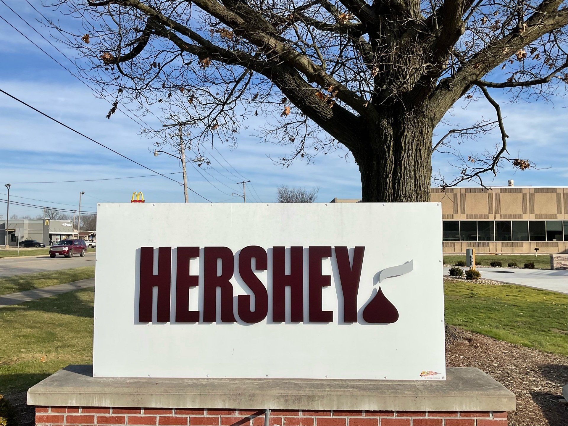 Hershey sign in brown and white; a tree and building are in the background.