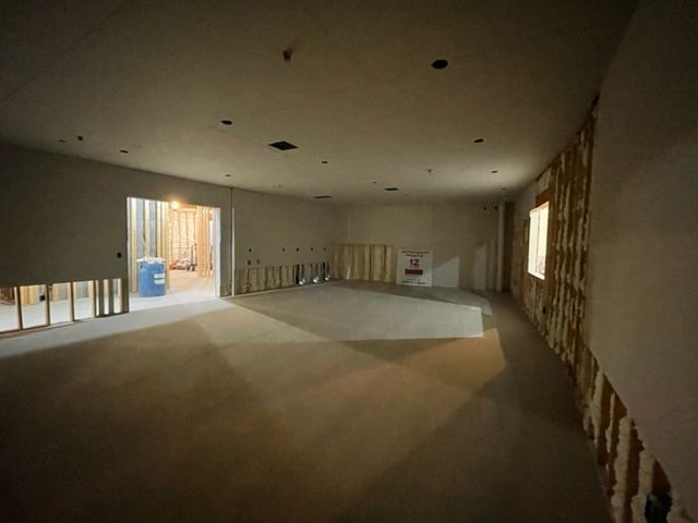 Interior of a room under construction, with exposed wooden studs, drywall, and a concrete floor.
