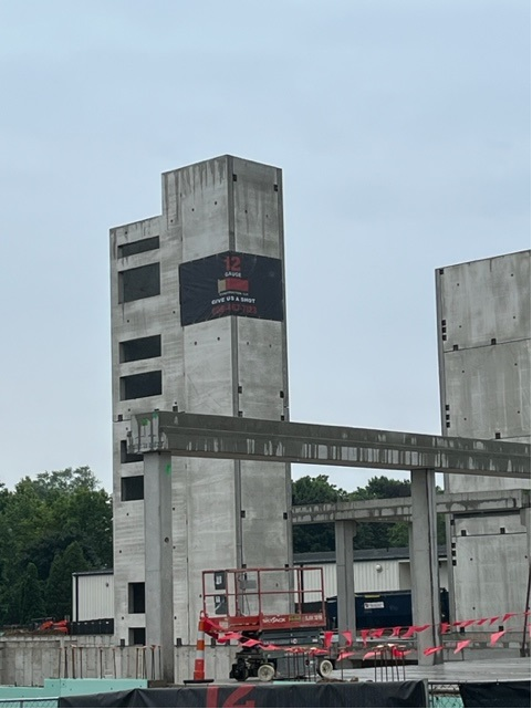 Concrete building under construction with a black logo, red lift, and gray sky.