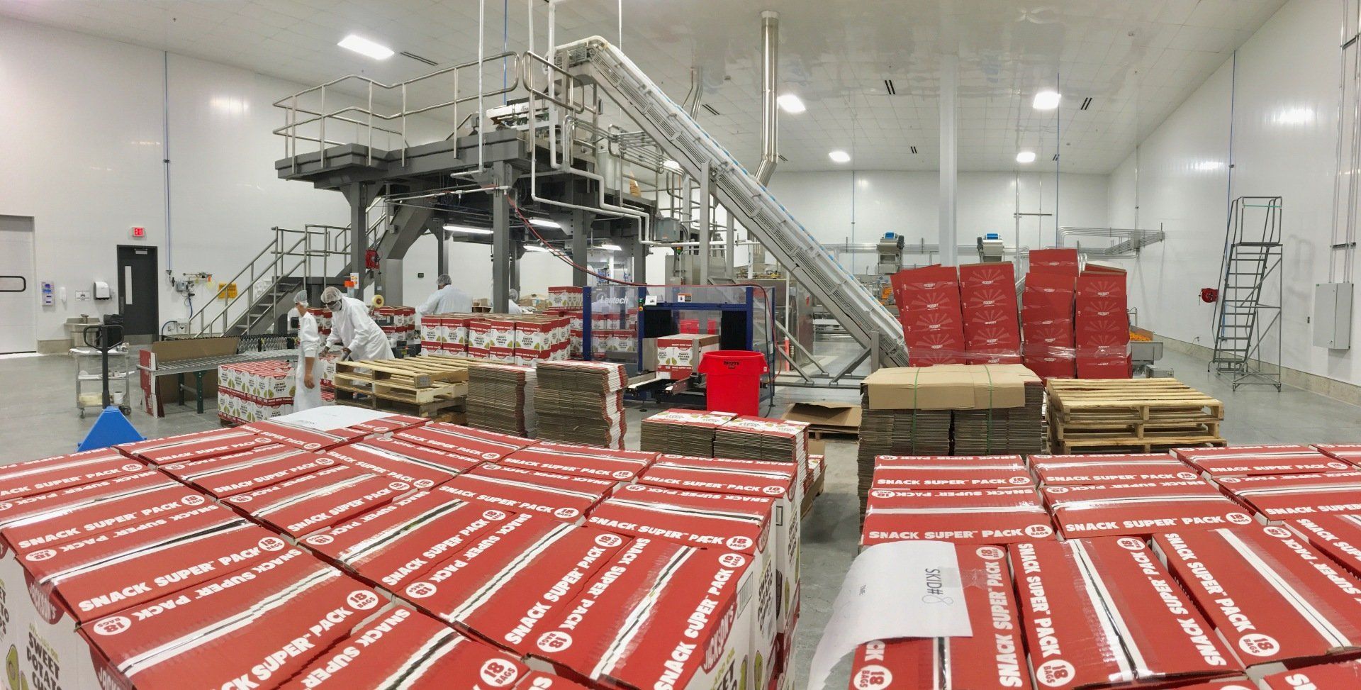 Warehouse with stacked red and brown boxes; conveyor system; a person working.