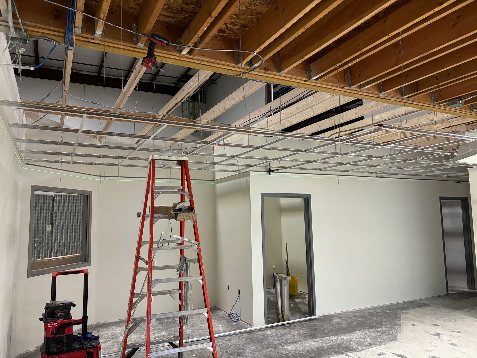 Interior renovation: unfinished ceiling, ladder, tools, white walls, doorway, and window.