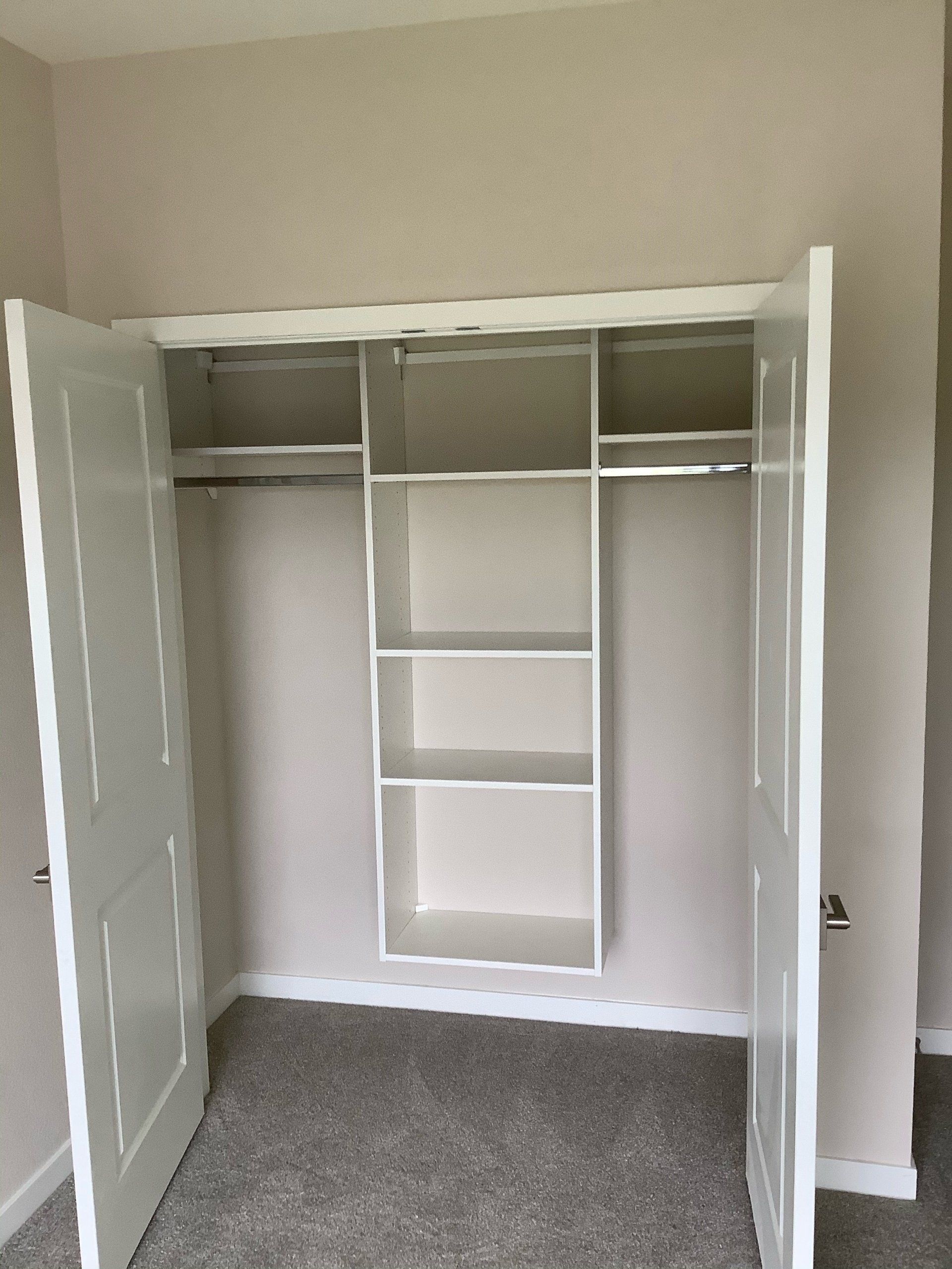 White closet with open doors, shelves, and a rod inside, set against a neutral wall and carpeted floor.
