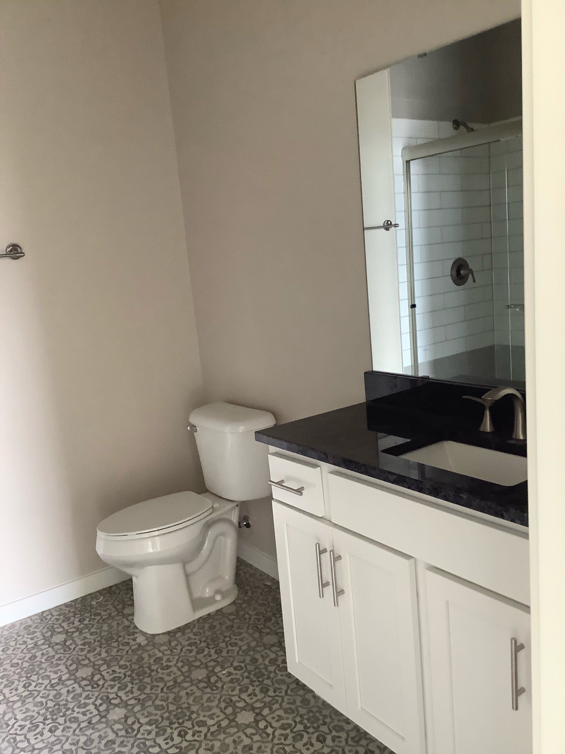 Bathroom with a white toilet, white vanity, and patterned floor. Large mirror.