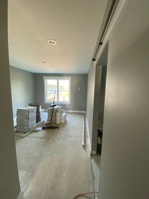 Interior of a room under renovation; gray walls, stacks of tiles, window, door frame, and unfinished floor.