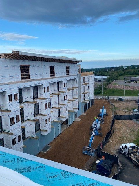 Multi-story apartment building under construction, exterior view. Blue sky background. Construction equipment visible.