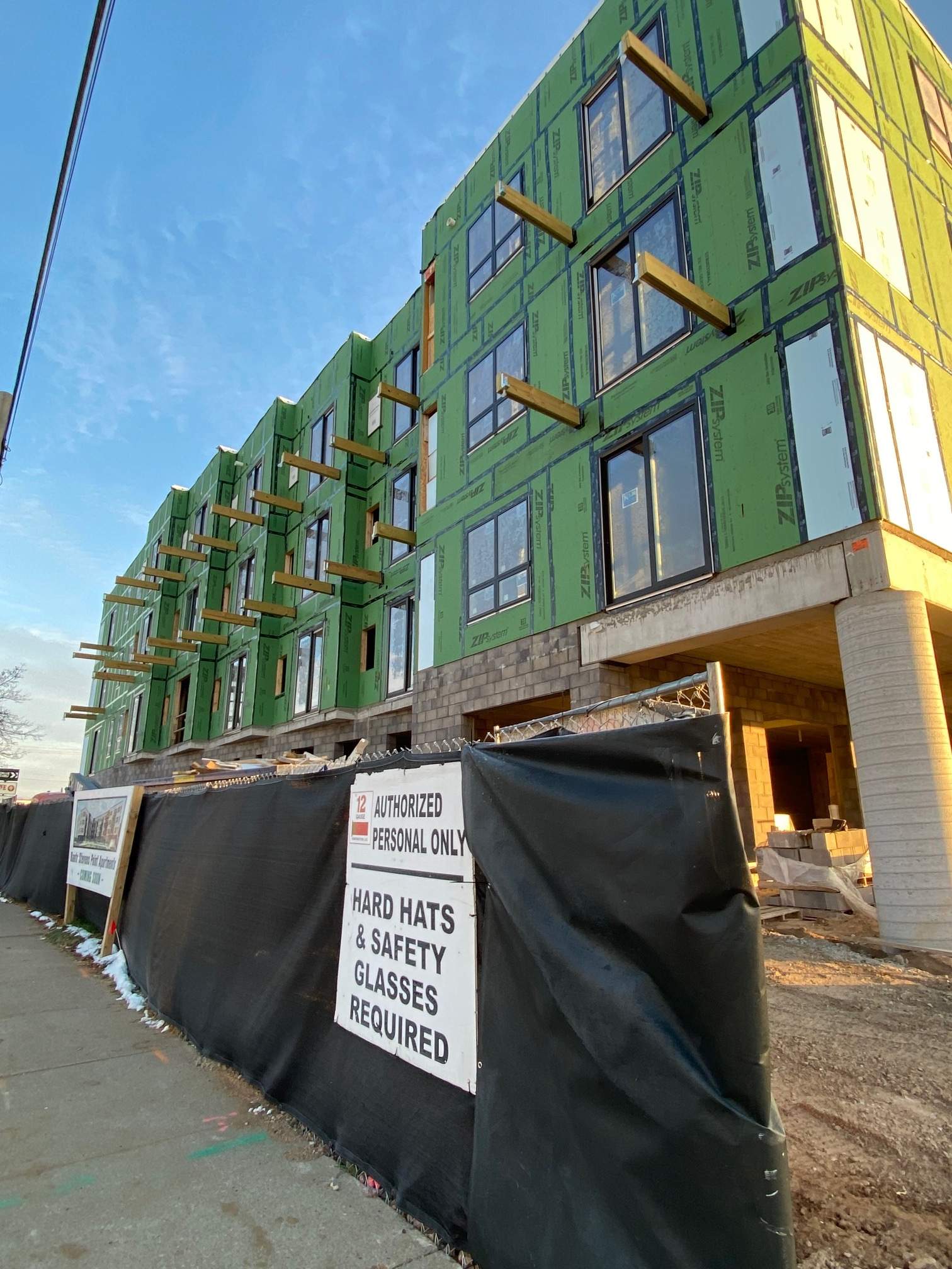 Construction site with a multi-story building under construction, black fence, hard hats and safety glasses required sign.