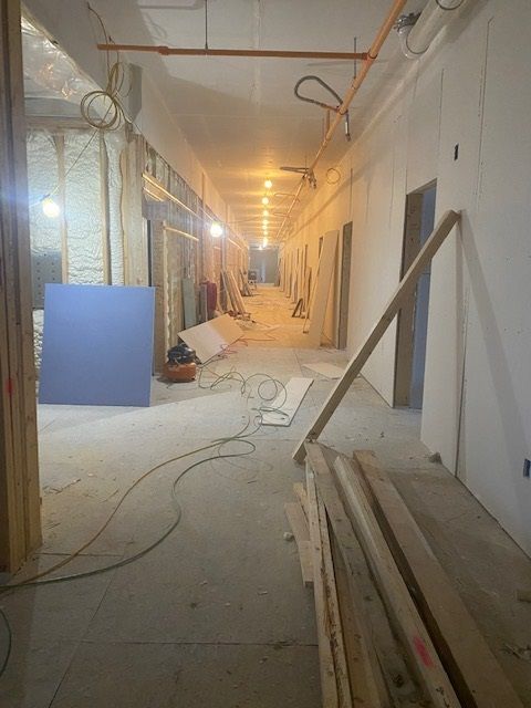 Construction site hallway; drywall installed. Wood and tools scattered. Fluorescent lighting.