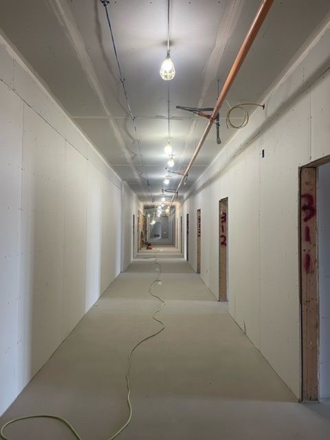 Empty hallway under construction, with overhead lights, exposed pipes, and doorways.