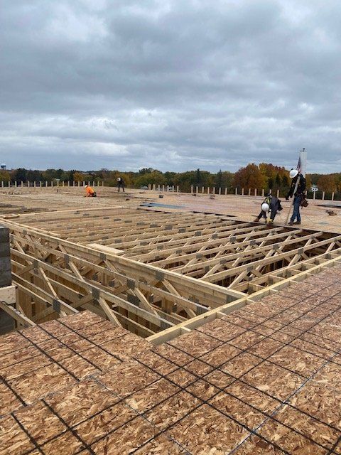 Construction workers on a rooftop installing wooden beams and decking under a cloudy sky.