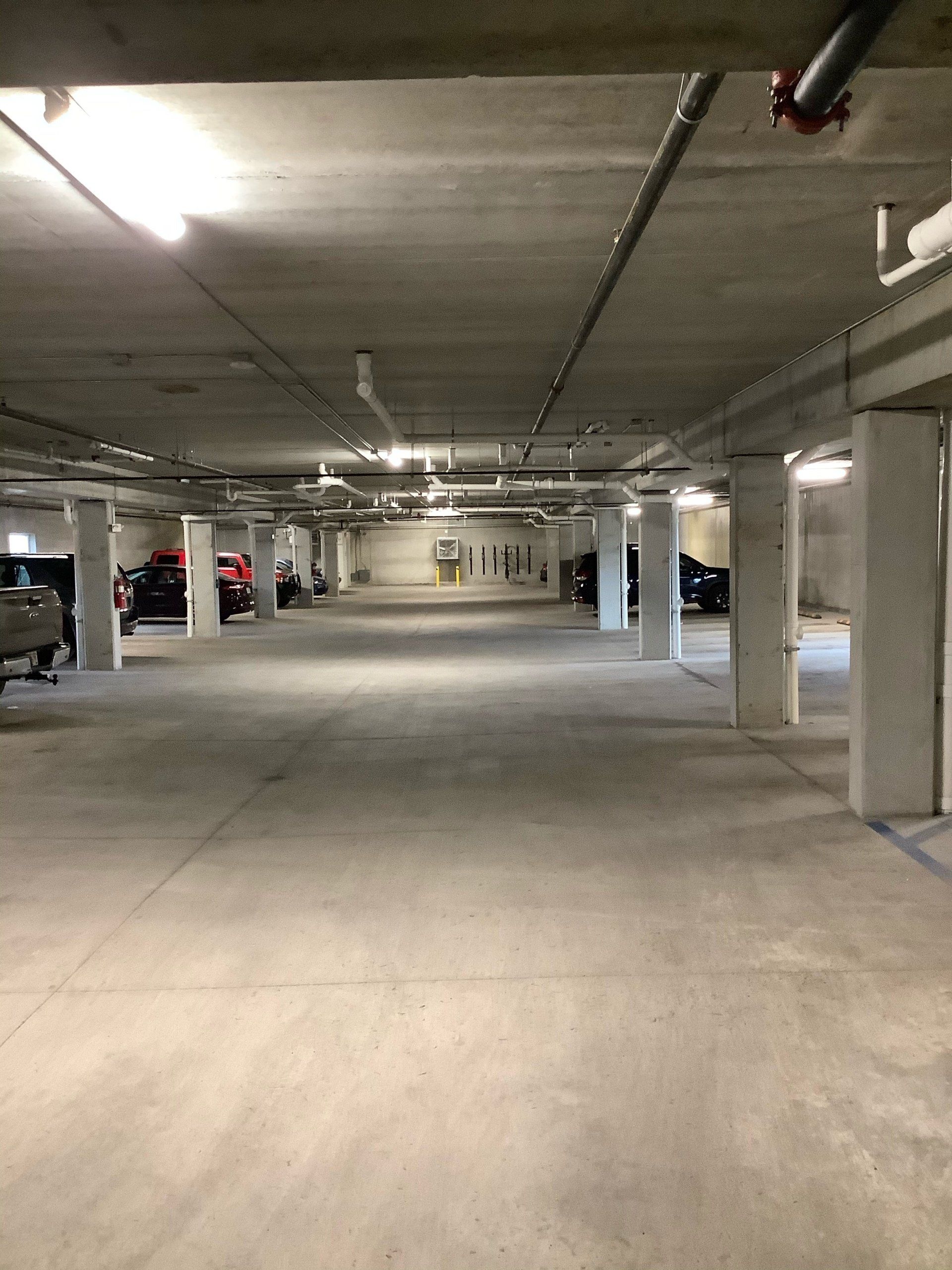 Concrete parking garage with cars parked in stalls; overhead lighting.