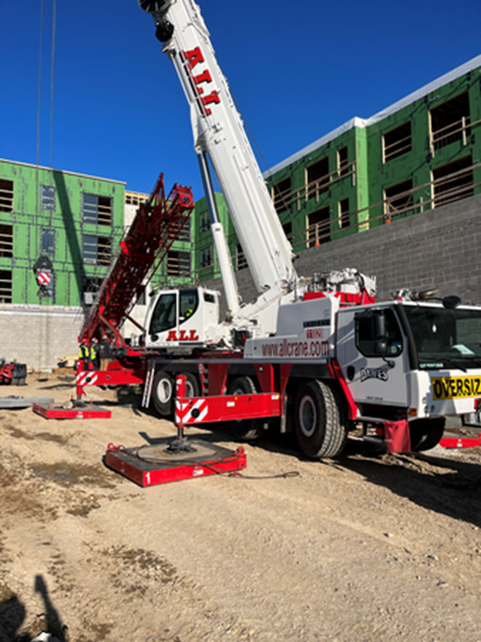 A large white and red crane on a construction site next to a building. Sunny day.