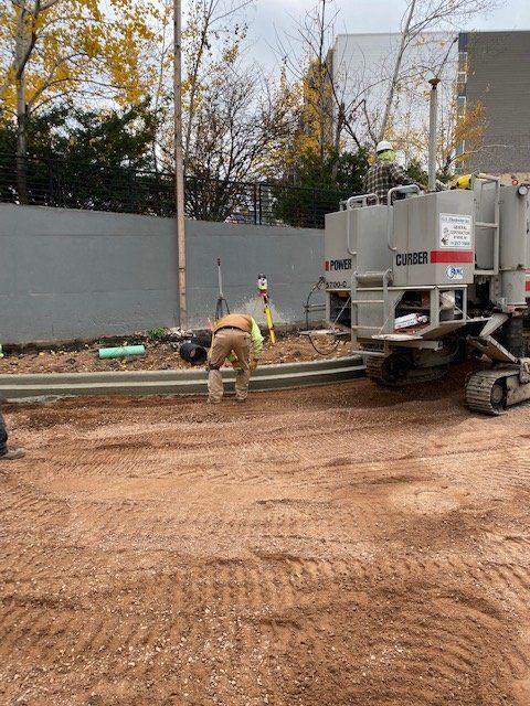 Construction workers with equipment laying concrete curb outdoors.