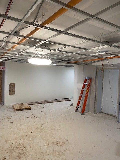 Construction in progress: Room with exposed ceiling grid, drywall, ladder, and debris on floor.