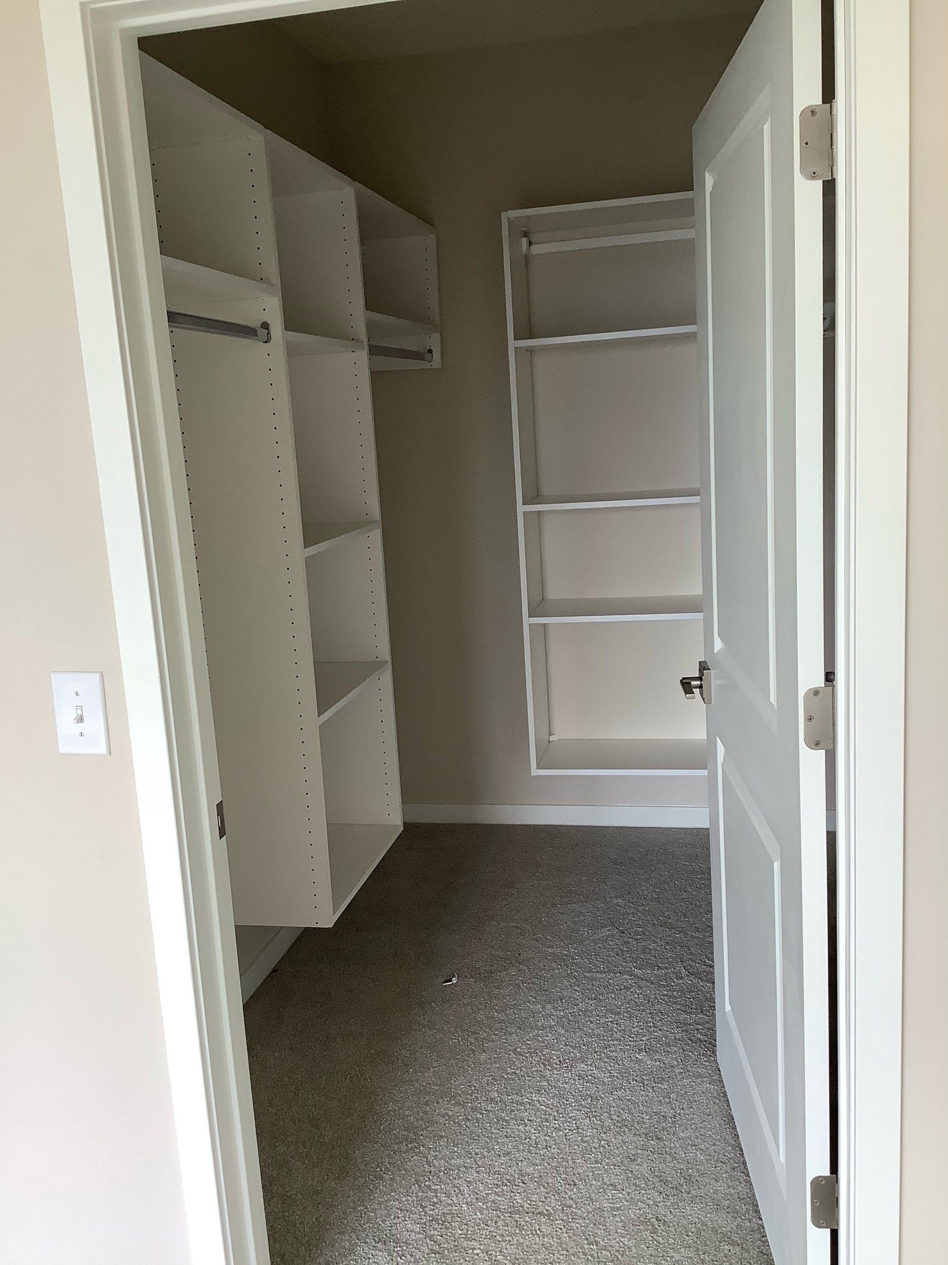 Walk-in closet with white shelves and door, gray carpet. Empty and well-lit.
