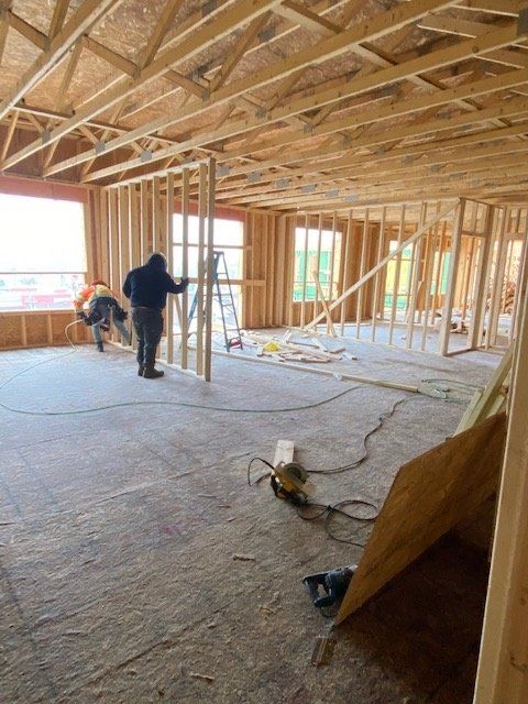 Construction workers framing interior walls and ceiling in a room with windows and unfinished flooring.
