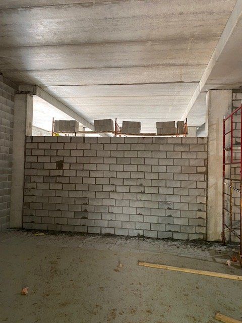 Interior view of unfinished construction with a gray brick wall. Concrete ceiling and support columns are visible.