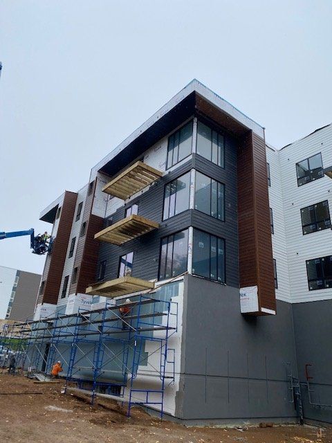 Apartment building under construction; exterior with gray and brown siding, scaffolding, large windows.