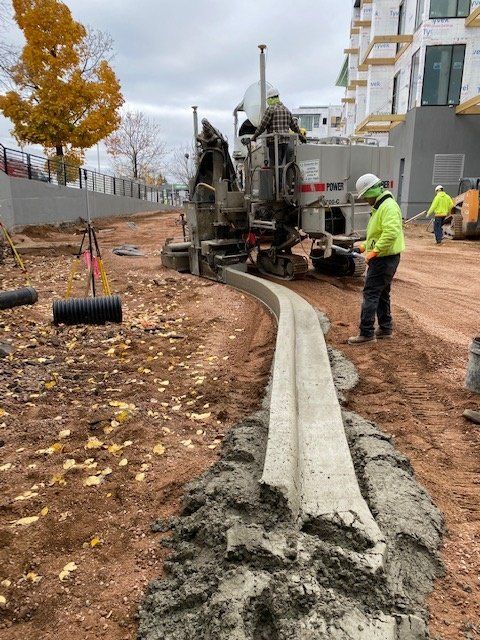 Construction workers pouring concrete curb using a cement truck on a construction site.