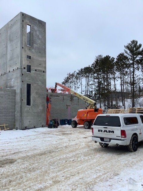 Construction site with concrete walls and an orange lift. A white pickup truck is parked in the snow.
