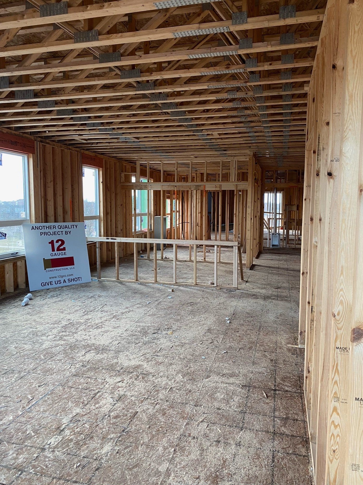 Interior view of a building under construction, showing wooden framing and flooring, with visible windows.