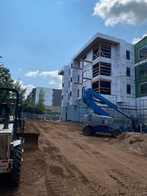 Construction site with a partially built apartment building, blue lift, and dirt path.