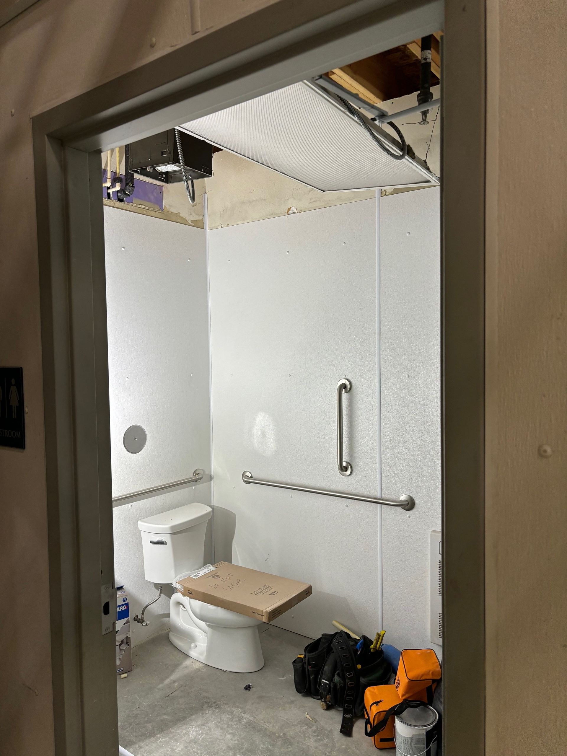 Bathroom interior with white walls, toilet, grab bars, and construction debris.