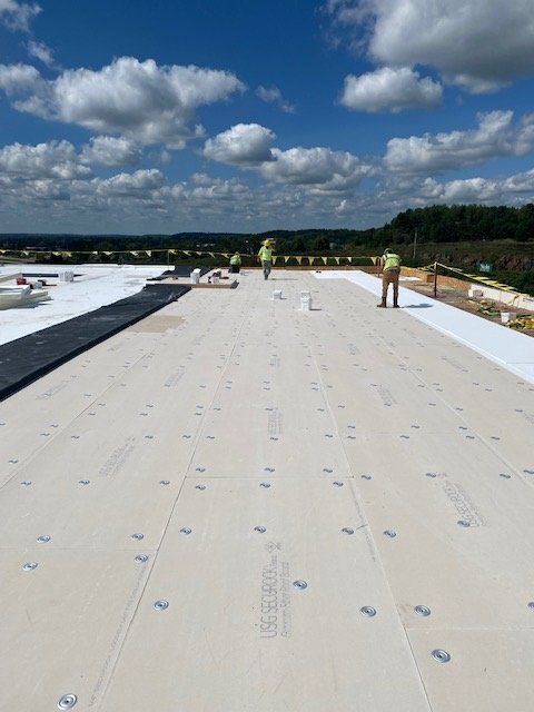 Workers on a rooftop install insulation under a bright blue sky with scattered clouds.