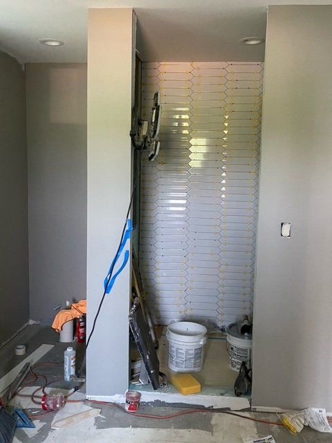 Bathroom renovation in progress; white tiled shower niche, gray walls, tools and supplies on the floor.