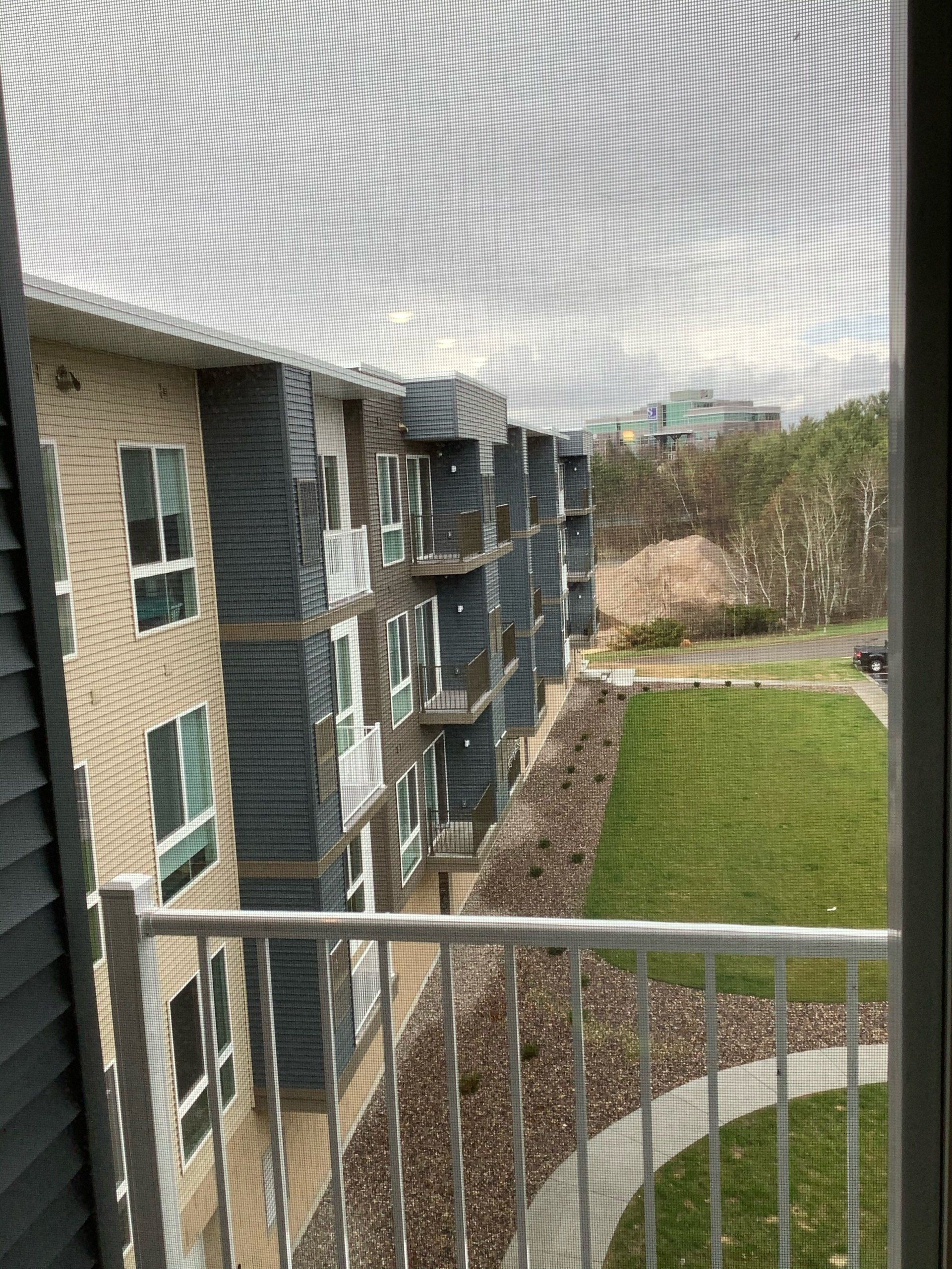 View from balcony of an apartment building with several balconies and green space below.