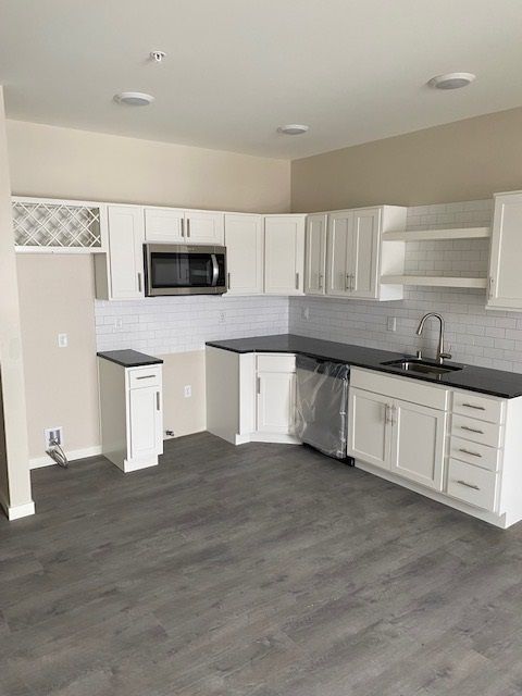 White kitchen cabinets, black countertops, stainless steel appliances, and gray flooring.
