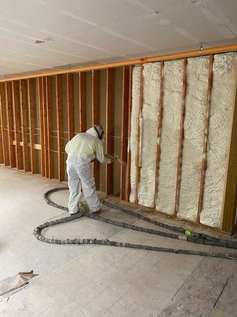 Worker in protective suit sprays foam insulation into a wall frame.