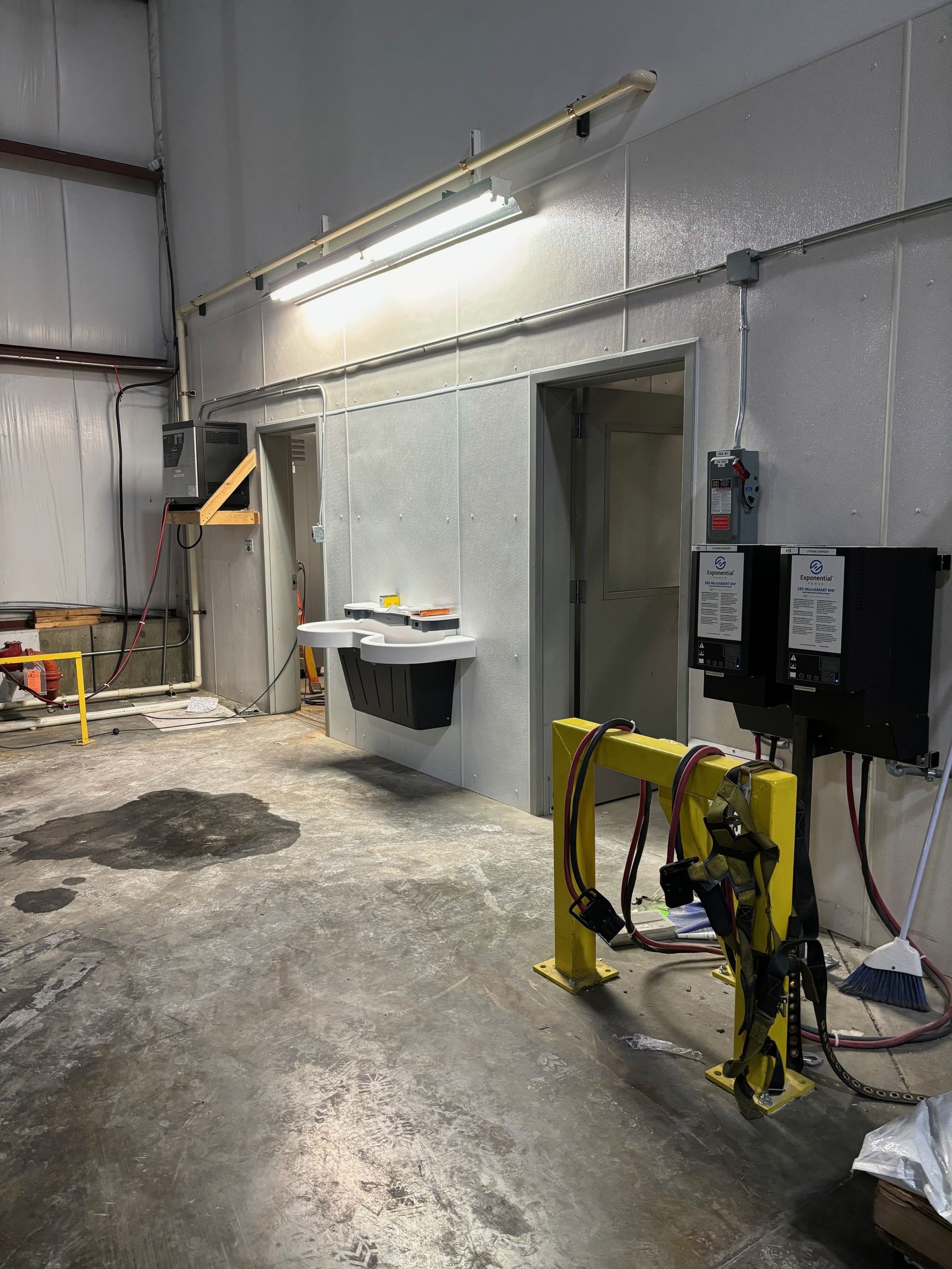 Industrial interior with grey walls, doors, overhead lighting, and yellow equipment.