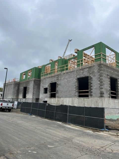 Construction site with concrete block building in progress, unfinished upper levels with wooden framing, cloudy sky.