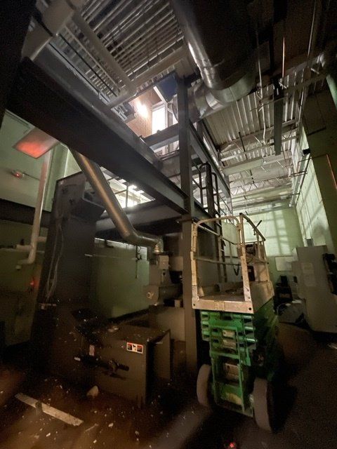 Interior view of industrial space with machinery and a green lift; ceiling is open.
