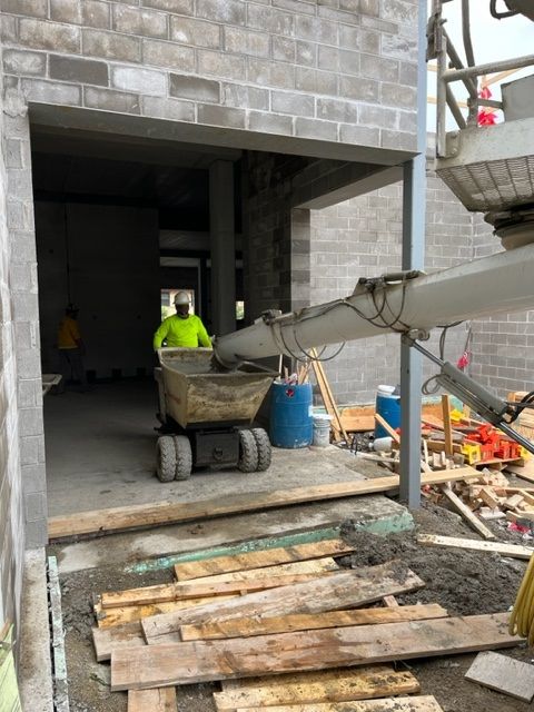 Construction worker using a motorized wheelbarrow to receive concrete from a spout. Setting is a building doorway.